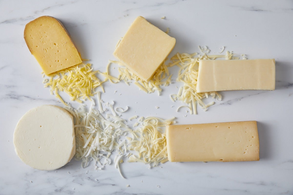 Blocks of different types of cheese on a marble slab, some grated.